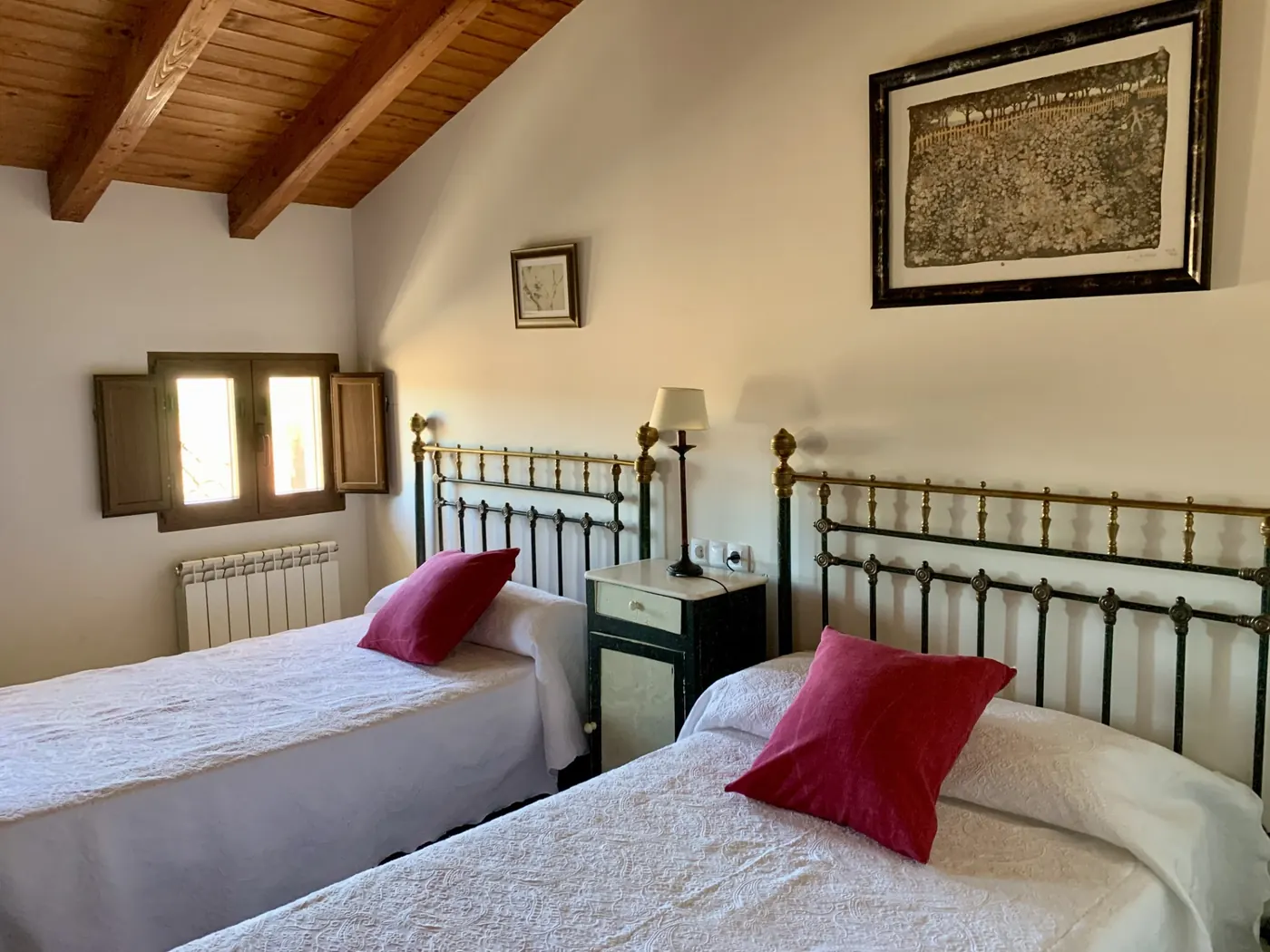Habitación con dos camas de forja y cojines rojos
